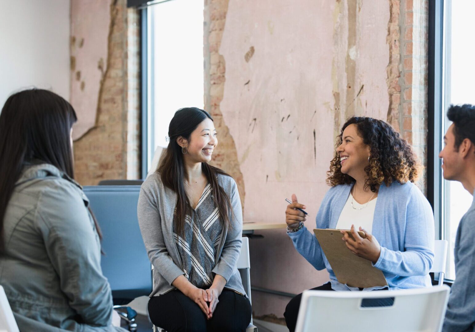 The mid adult female manager smiles and gestures as she leads a meeting for her diverse staff.
