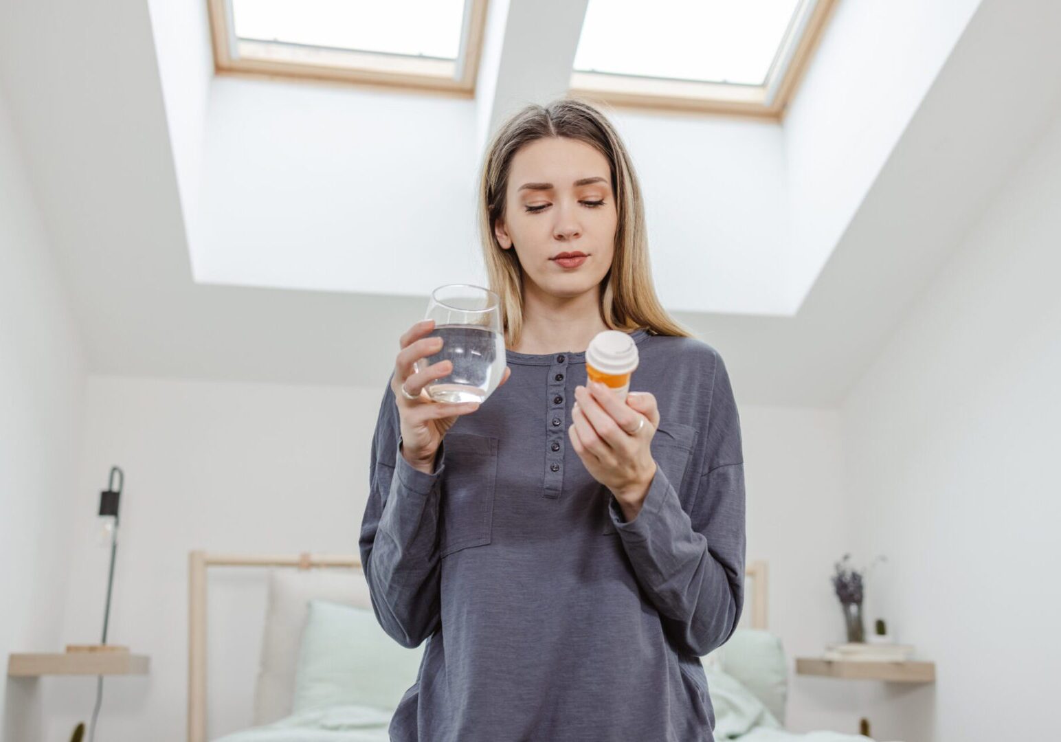Woman is holding a bottle of pills and glass of water