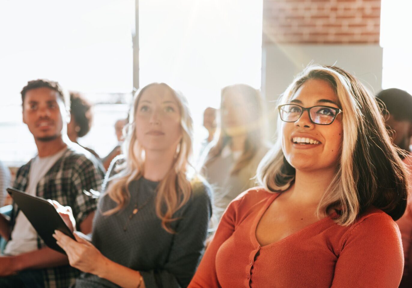 Diverse group of people, including a smiling woman, attending seminar. The seminar audience includes men and women of various ethnicities, all engaged in the seminar. Community seminar with audience.
