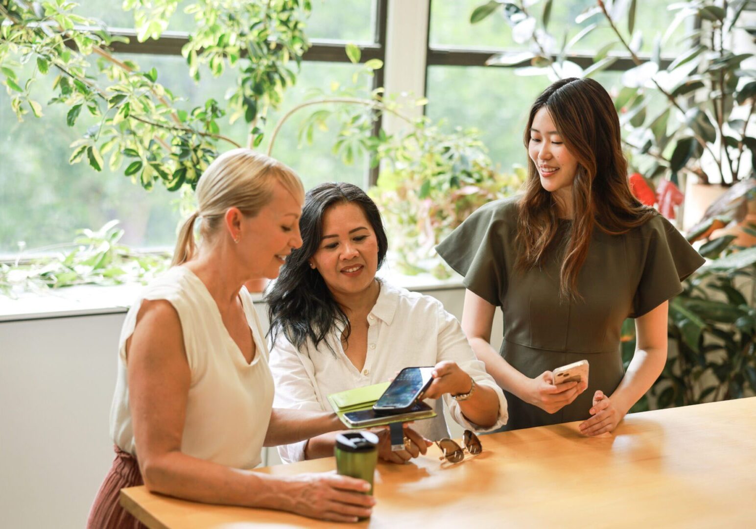A group of diverse multiracial business women are using a mobile and  working together and discussing a project in a sustainable office environment.